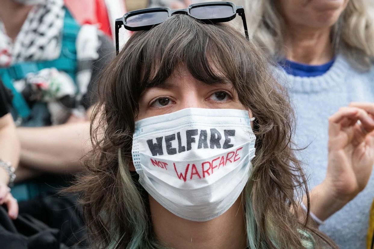 Person wearing a face mask with the words “Welfare not Warfare” written on it during a protest.
